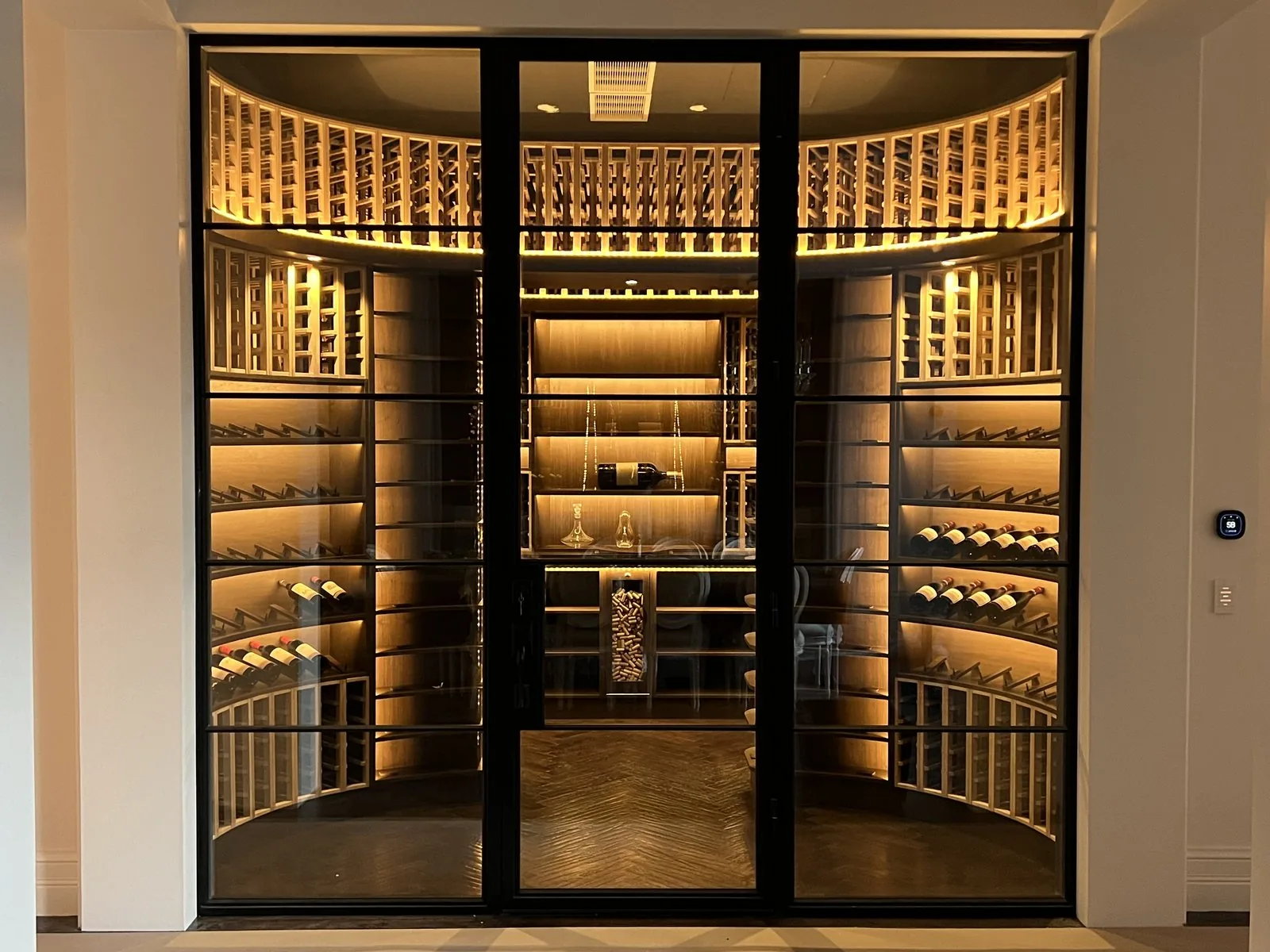 The finished, real curved wine cellar with glass doors and warm lighting
